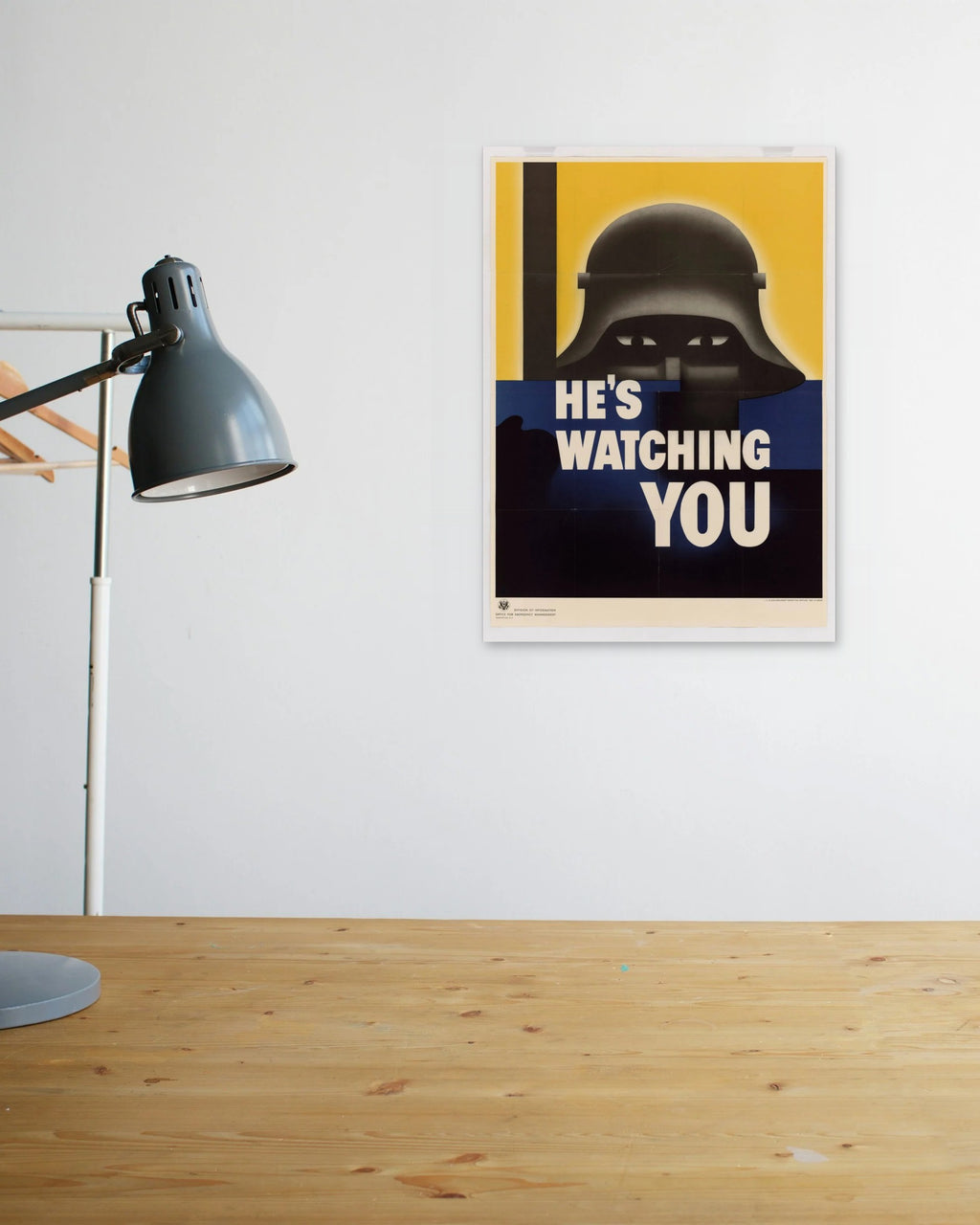 "He's Watching You" poster above a wooden desk