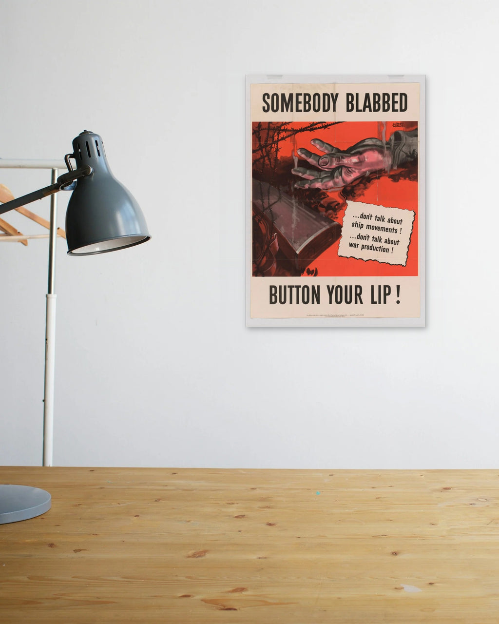 "Somebody Blabbed - Button Your Lip!" poster above a wooden desk